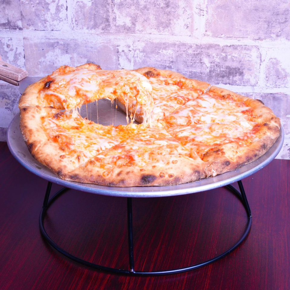 A slice of cheese pizza being lifted, showing melted cheese stretching, on a metal stand.