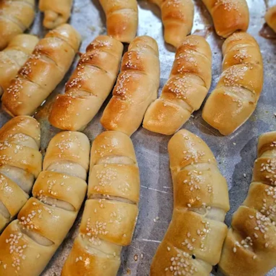 Close-up of golden-brown baked pastries, possibly cheese rolls or breadsticks, sprinkled with sesame seeds.